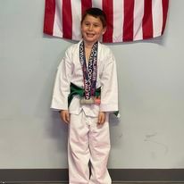 A young boy in a taekwondo uniform is standing in front of an american flag.
