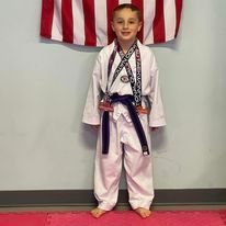 A young boy in a karate uniform is standing in front of an american flag.