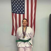 A woman in a karate uniform is standing in front of an american flag.
