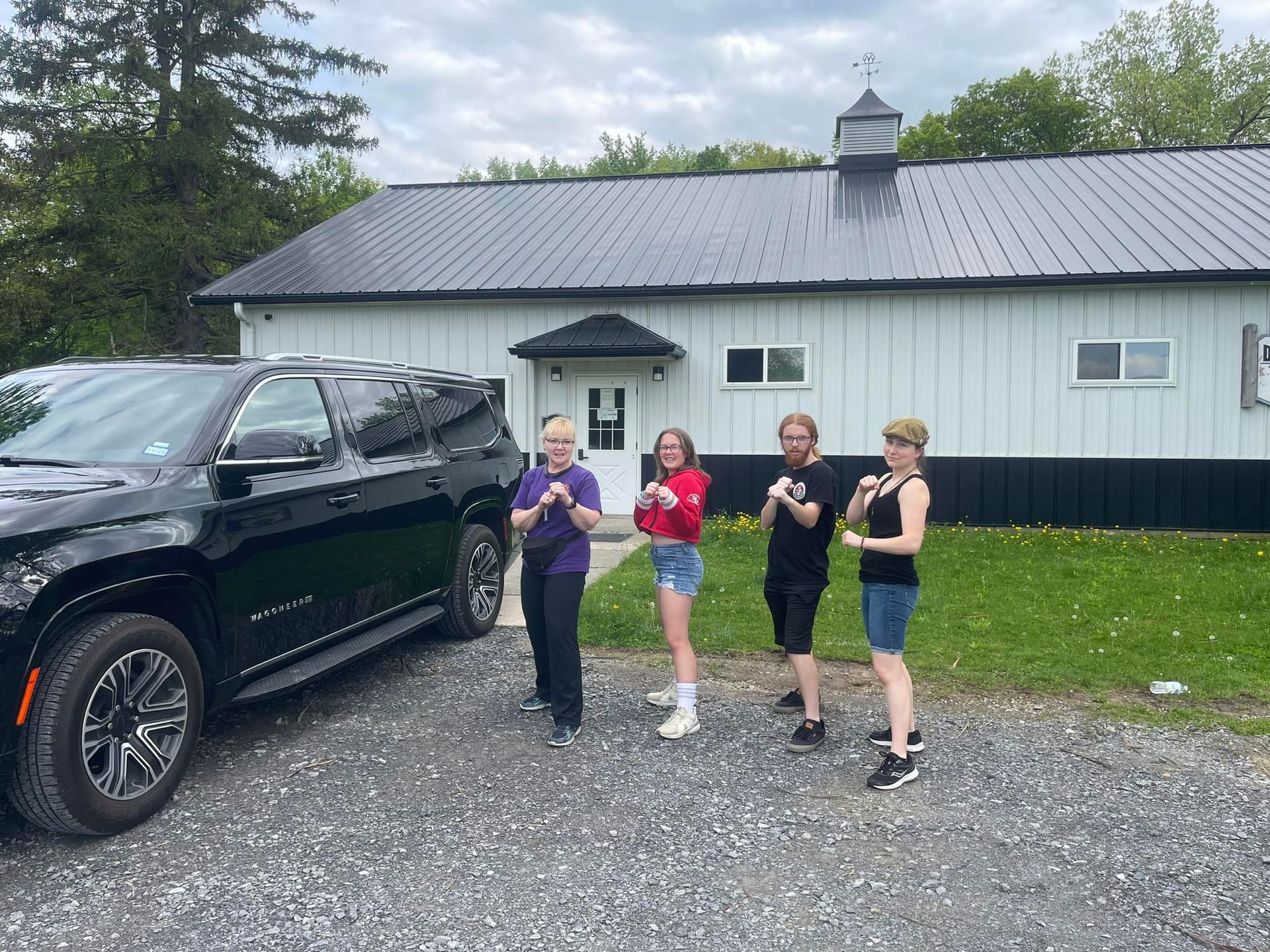 A group of people are standing in front of a black suv in a parking lot.