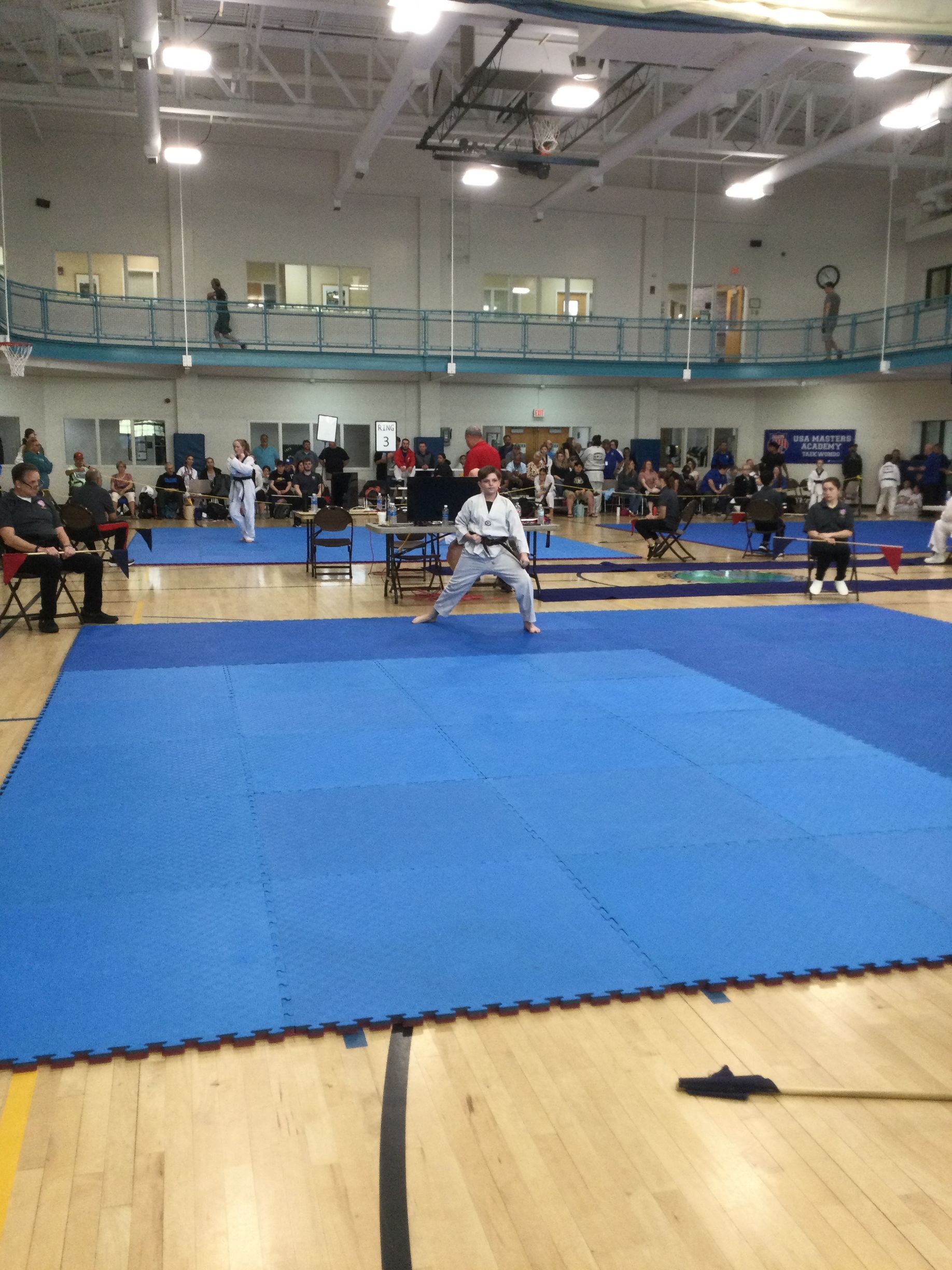 A man in a white karate uniform is standing on a blue mat in a gym