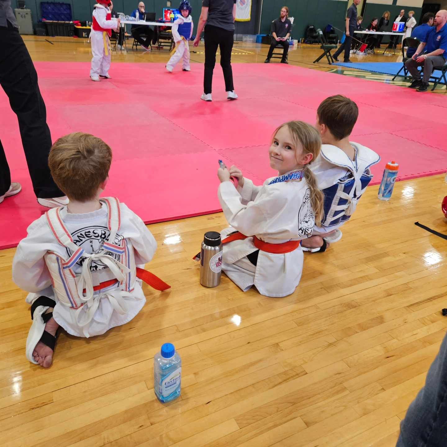 A group of kids are sitting on the floor in front of a karate mat