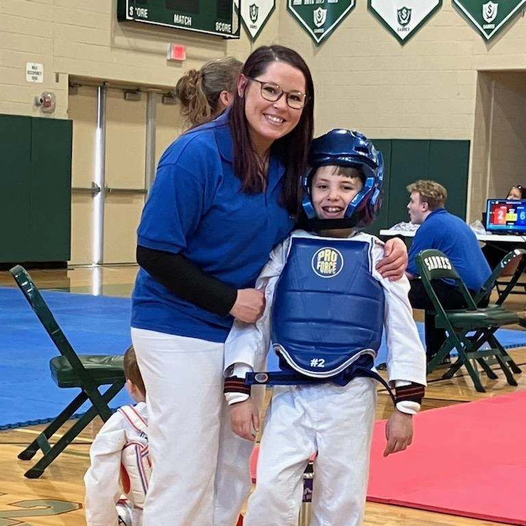 A woman in a blue shirt stands next to a young boy wearing a helmet