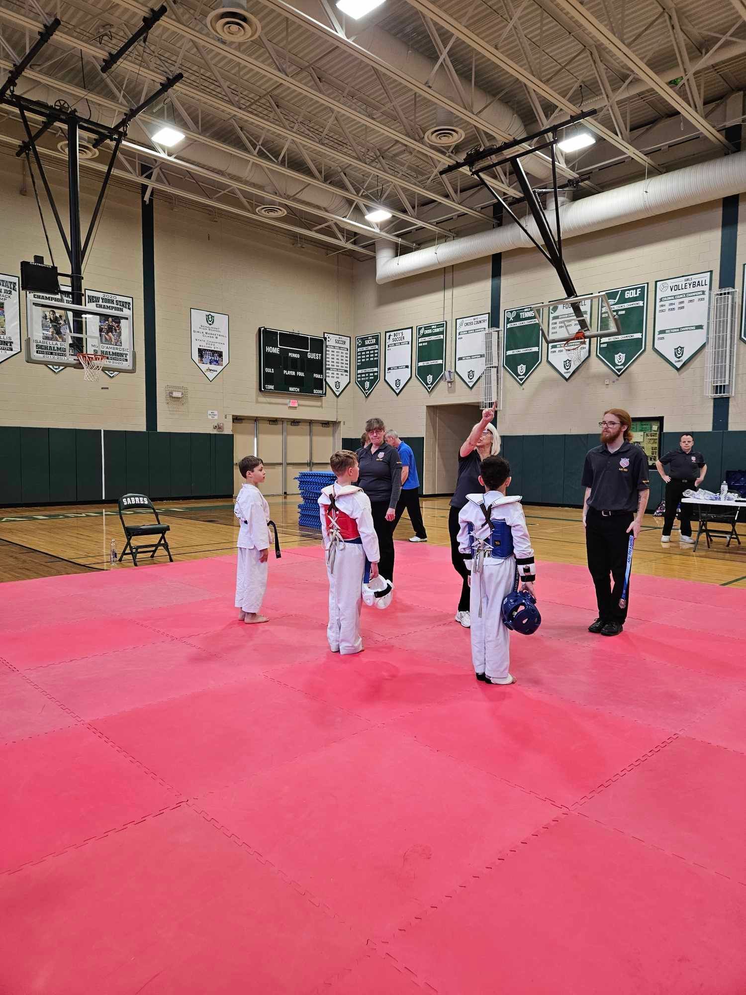 A group of people are standing on a red mat in a gym.