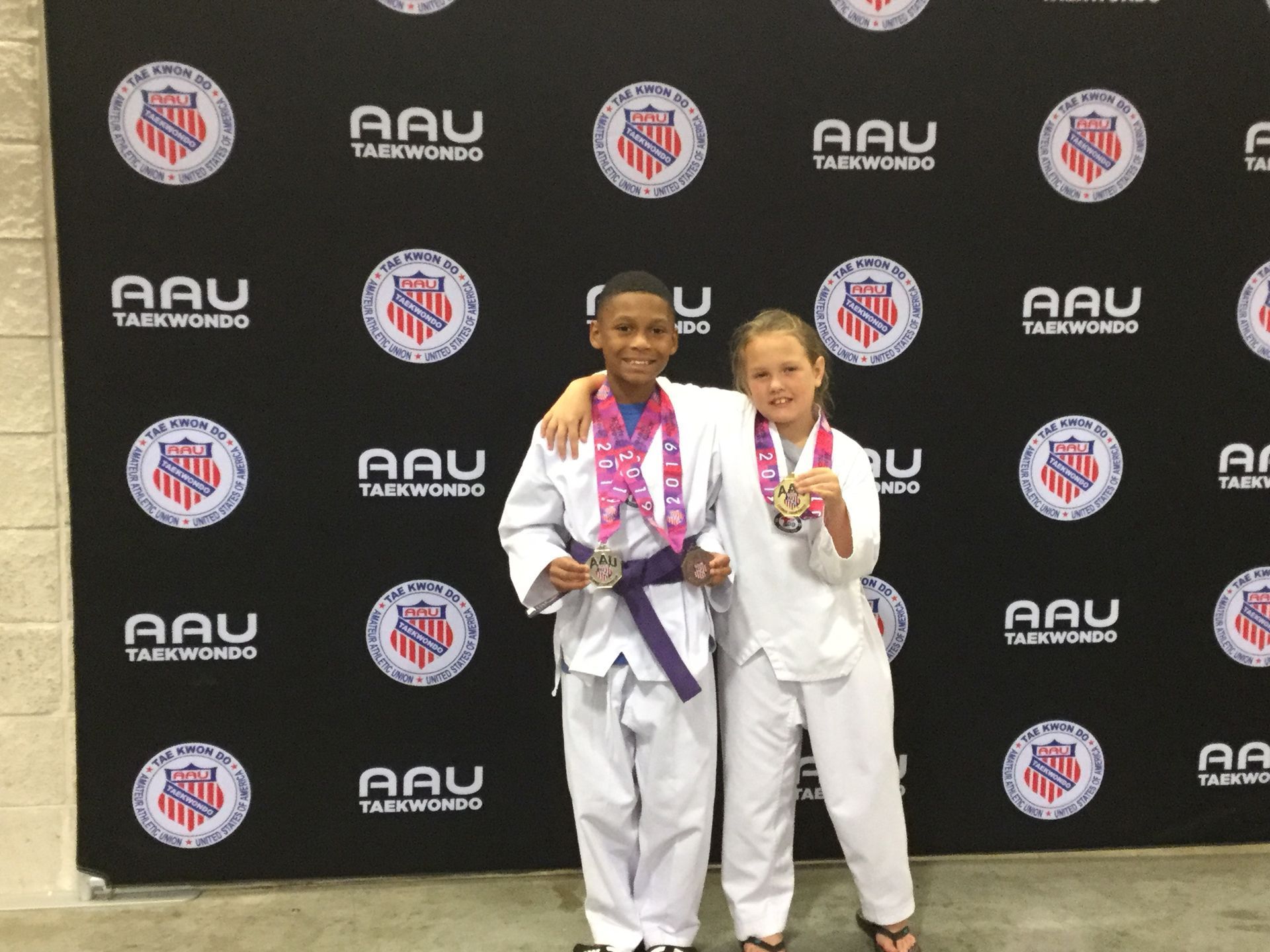 A boy and a girl standing in front of a wall that says aau