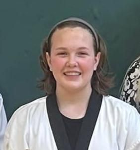 A young woman in a taekwondo uniform is smiling for the camera.