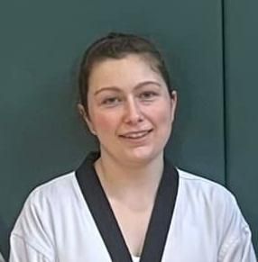 A woman in a white karate uniform with a black collar is smiling.