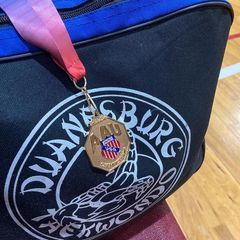 A medal is hanging from a blue bag on a wooden floor.