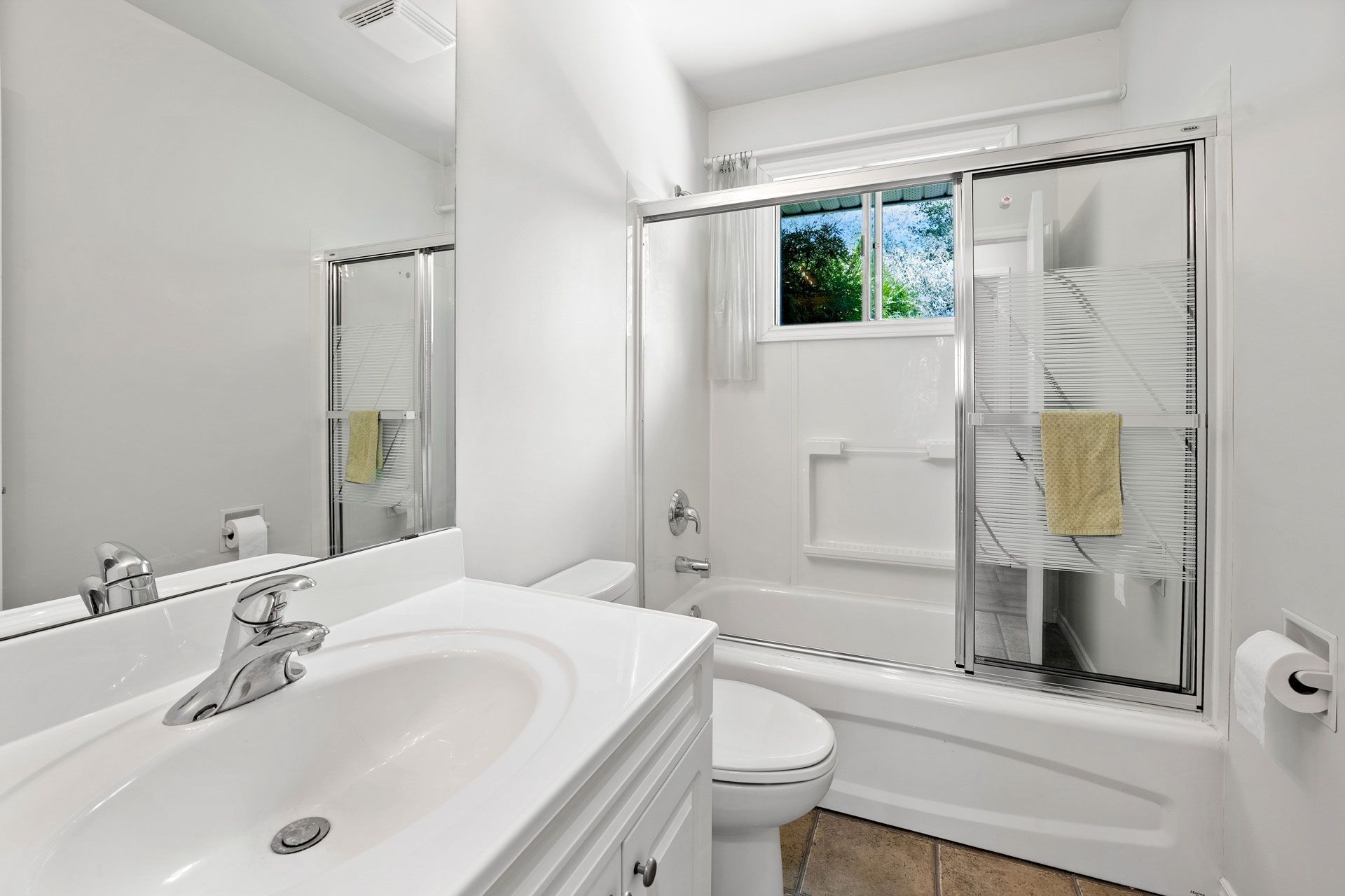 Bright white bathroom with a sink, toilet, tub/shower, and small window.