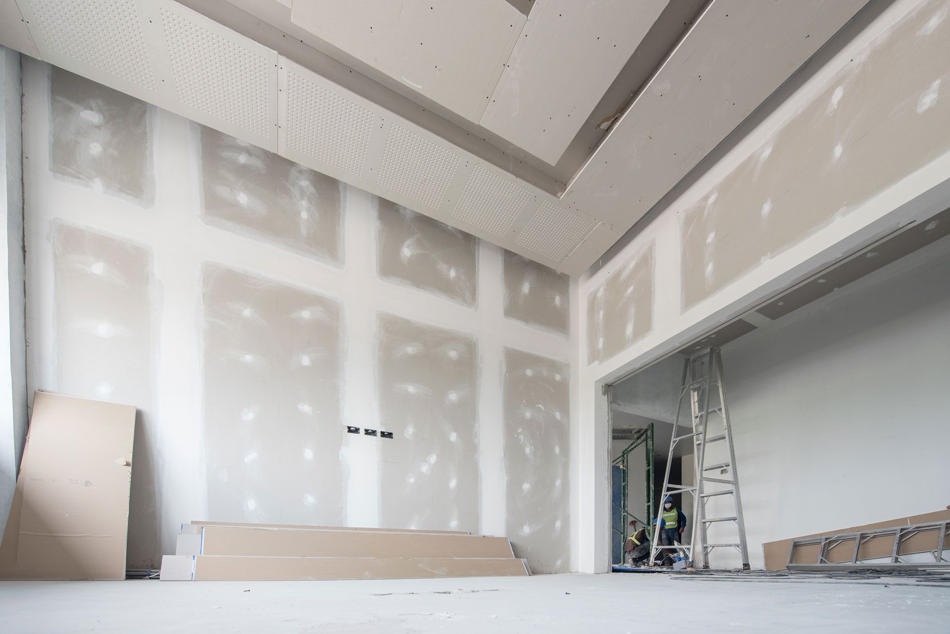 Interior of a room under construction, with drywall on walls and ceiling, ladder and materials visible.