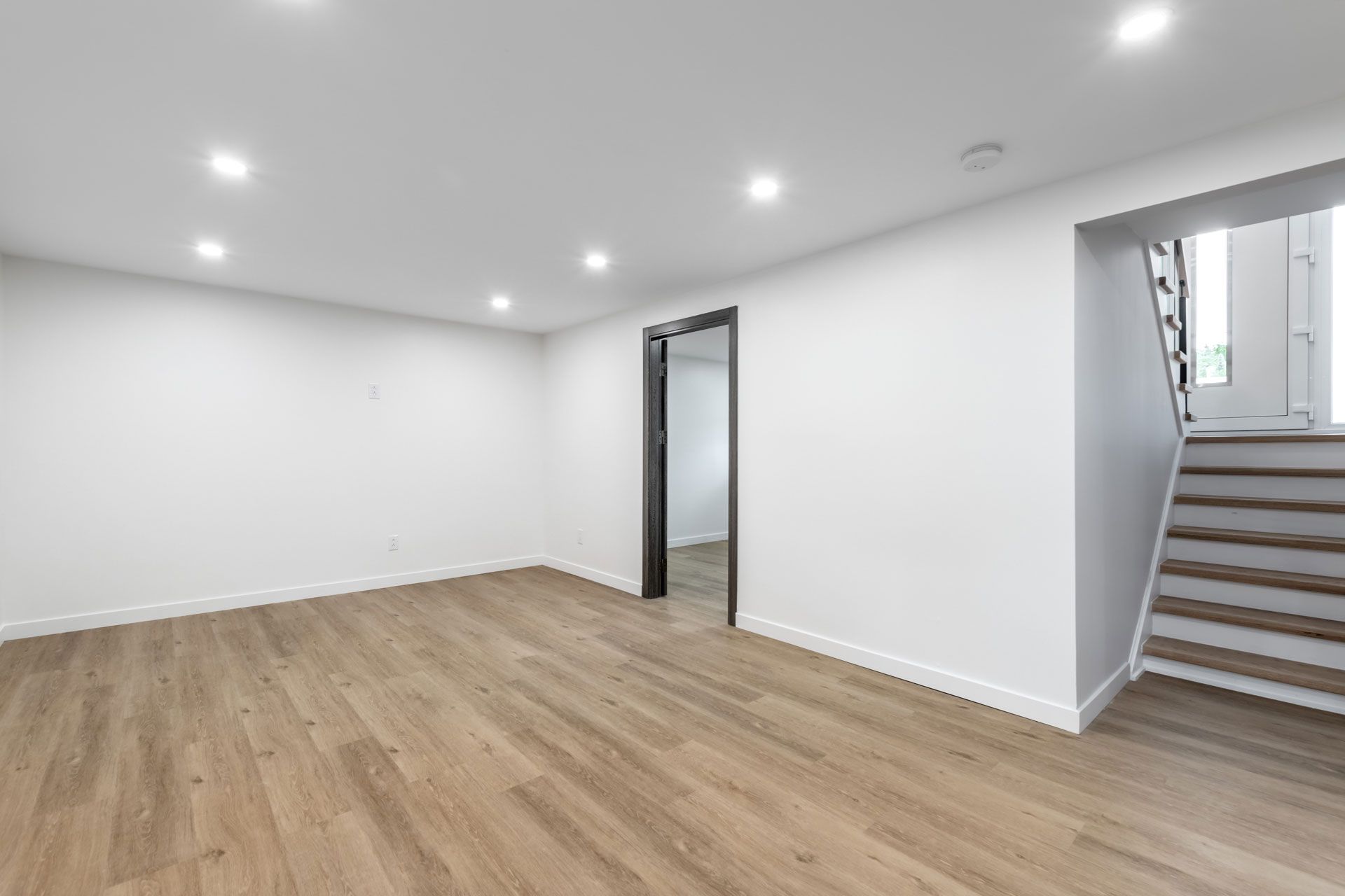 Empty room with wood floors, white walls, recessed lighting, and a staircase leading upwards.