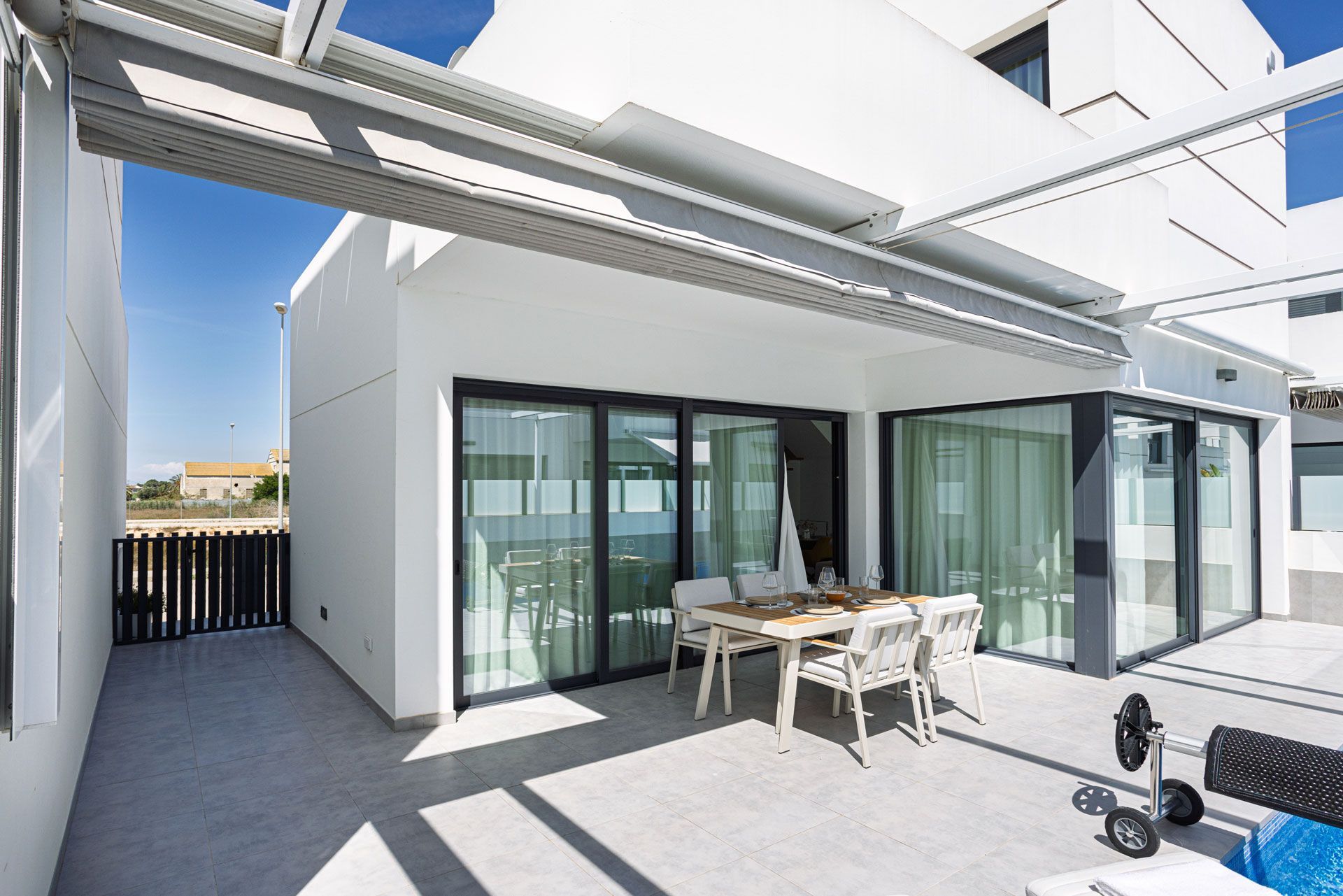 White patio with sliding glass doors, table, chairs, and metal awning on a sunny day.