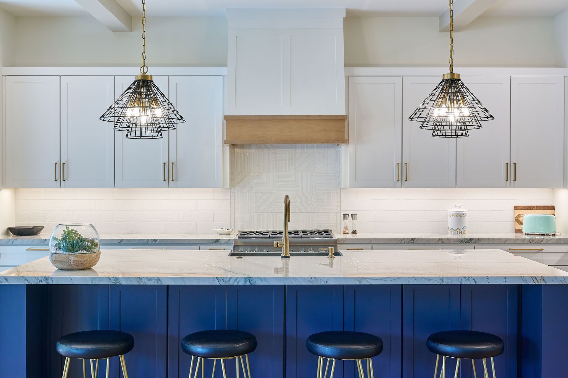 Kitchen with blue island, white cabinets, gold accents, and pendant lights.