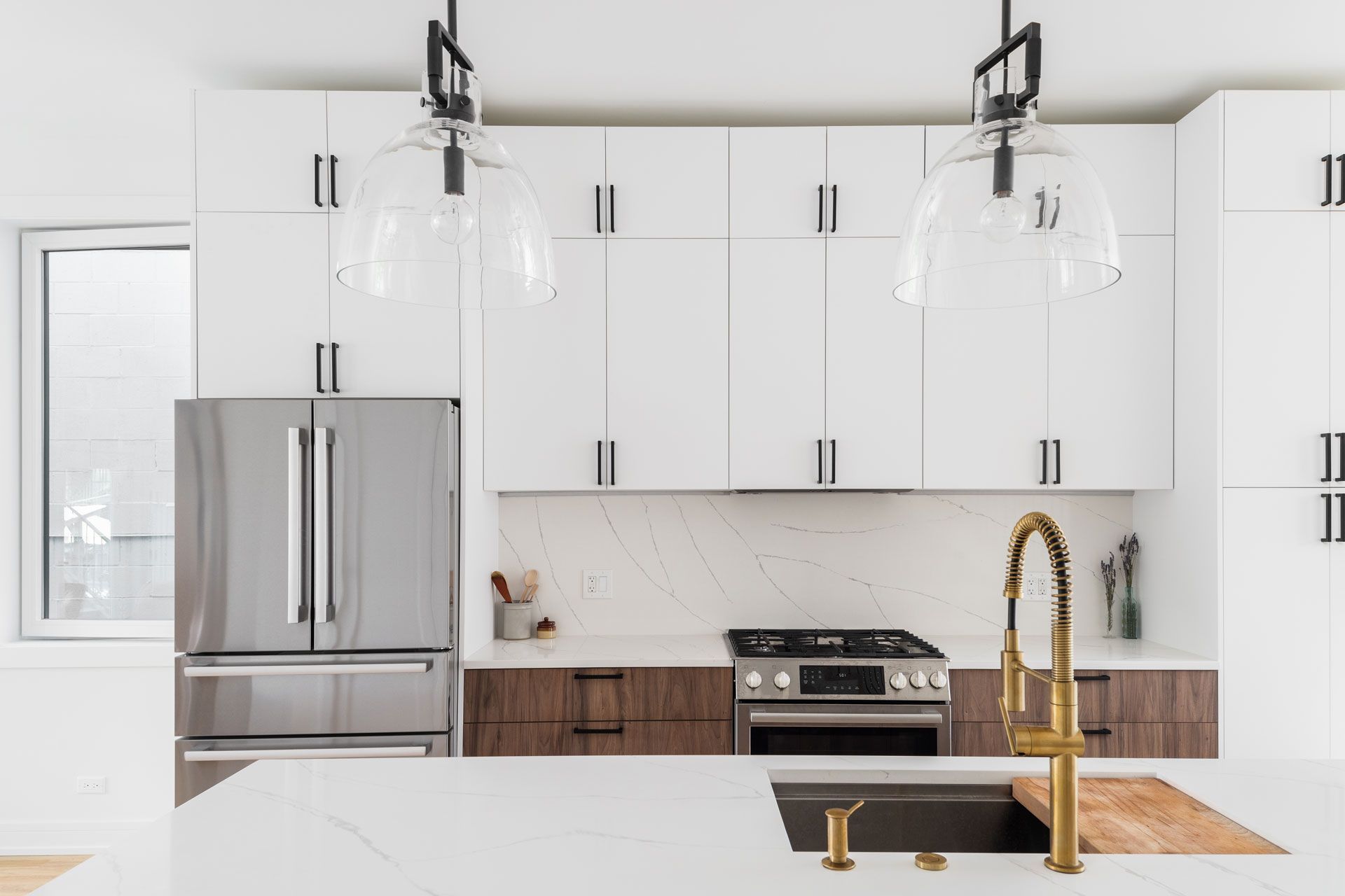Modern kitchen with white upper cabinets, stainless steel fridge, and gold faucet.