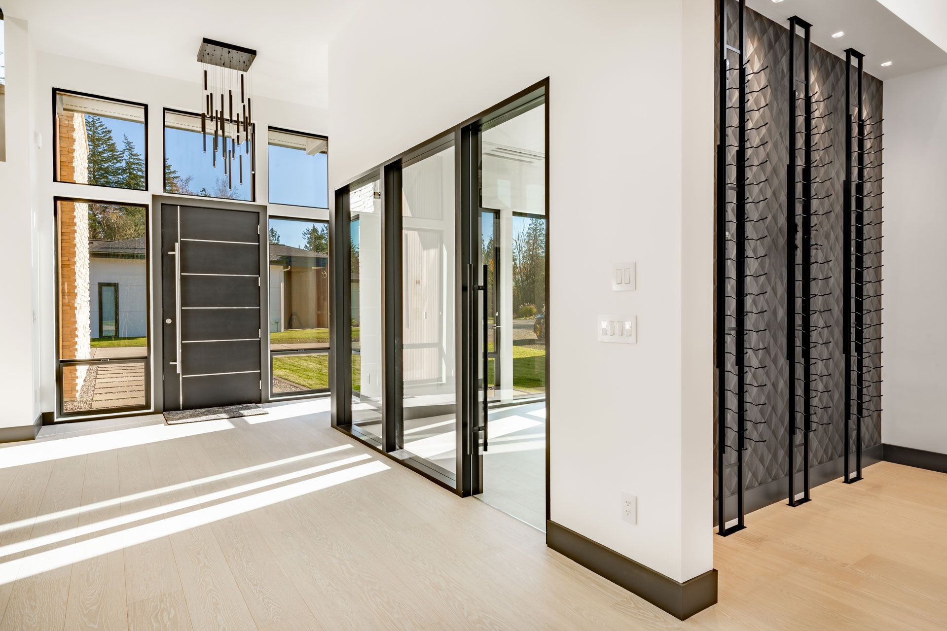 Modern home entryway with large windows, sliding glass doors, and decorative wall panel.