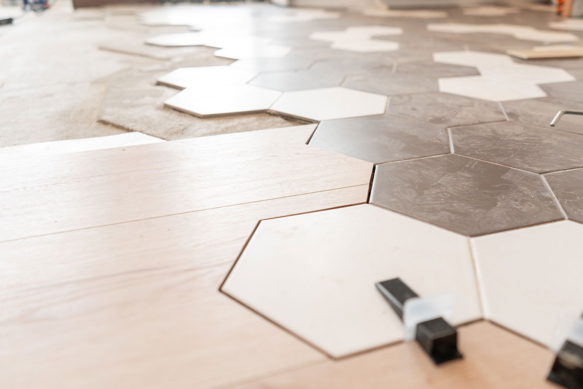 Installing hexagonal tiles on a floor, with wood and gray tiles interspersed.