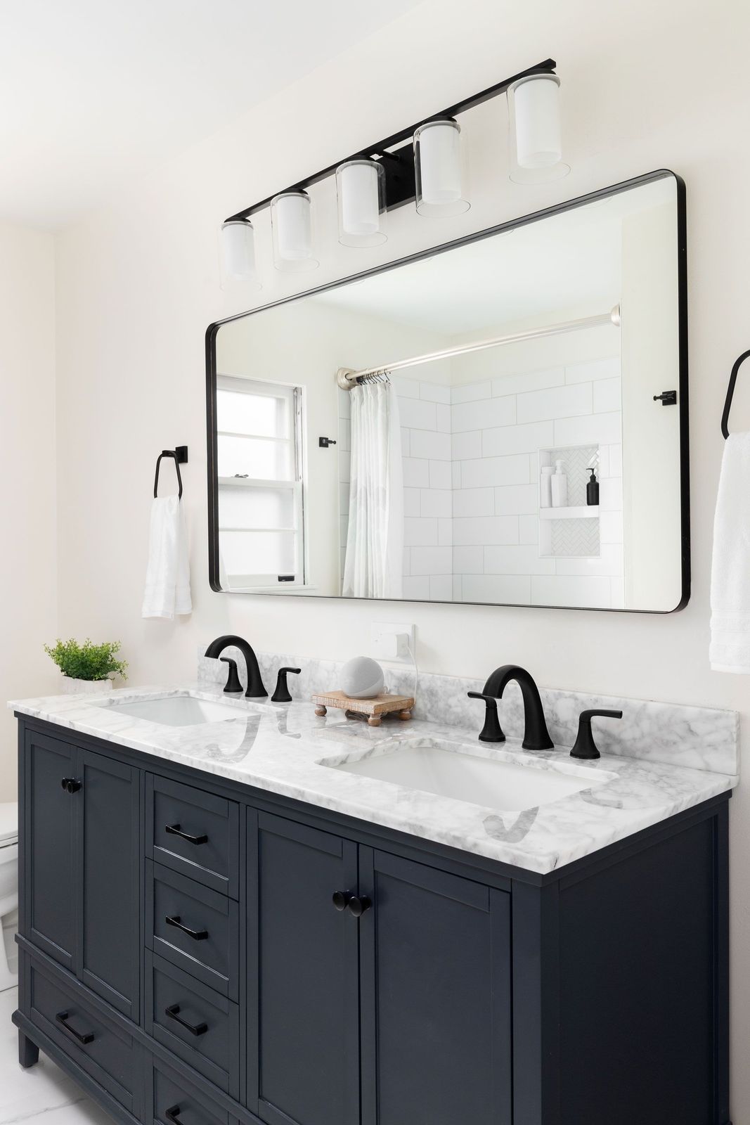 Navy blue double sink vanity with marble top, black fixtures, and large mirror in a bathroom.