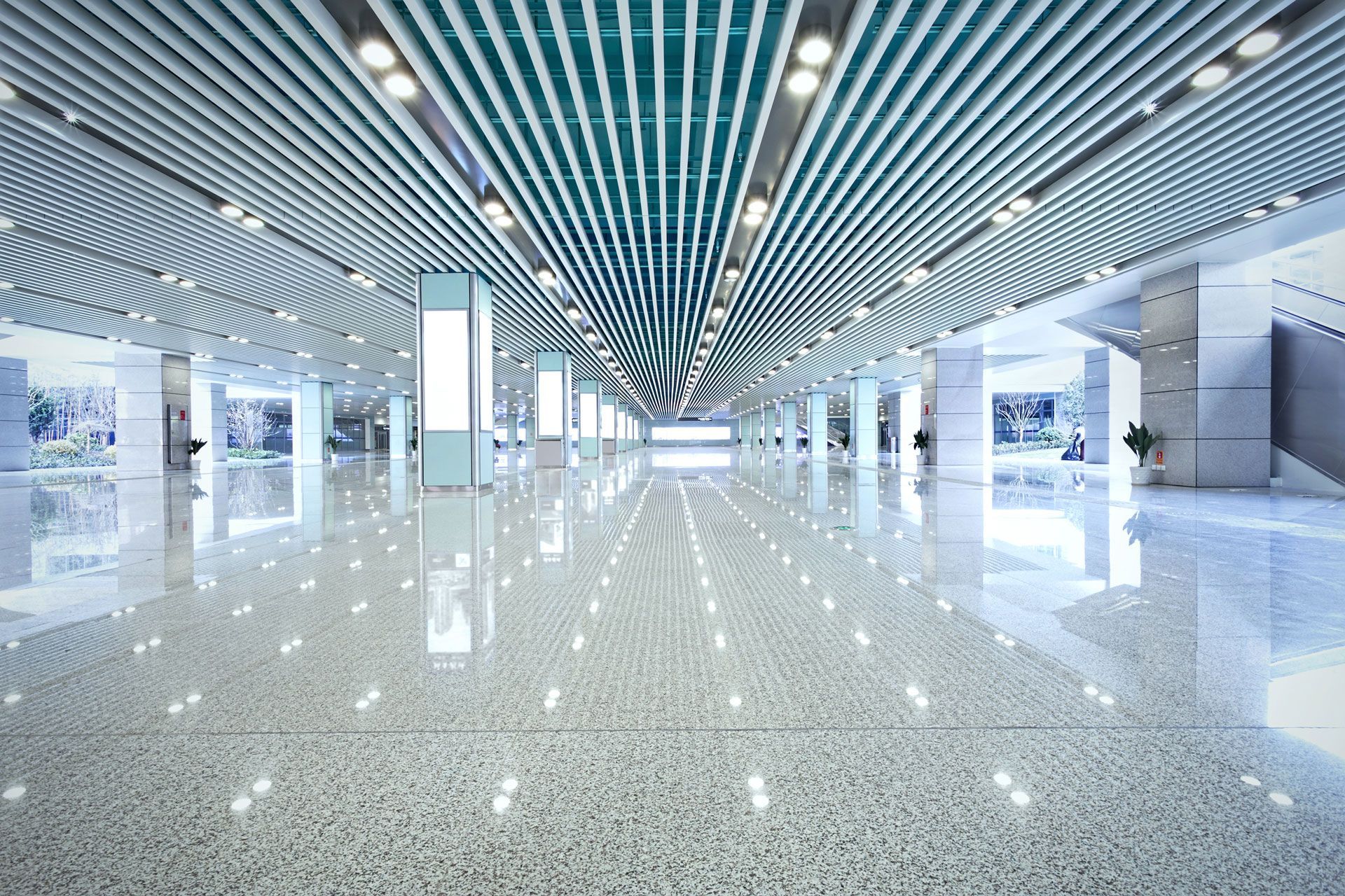 Wide, bright, modern hall with reflective white flooring and a curved, lined ceiling.