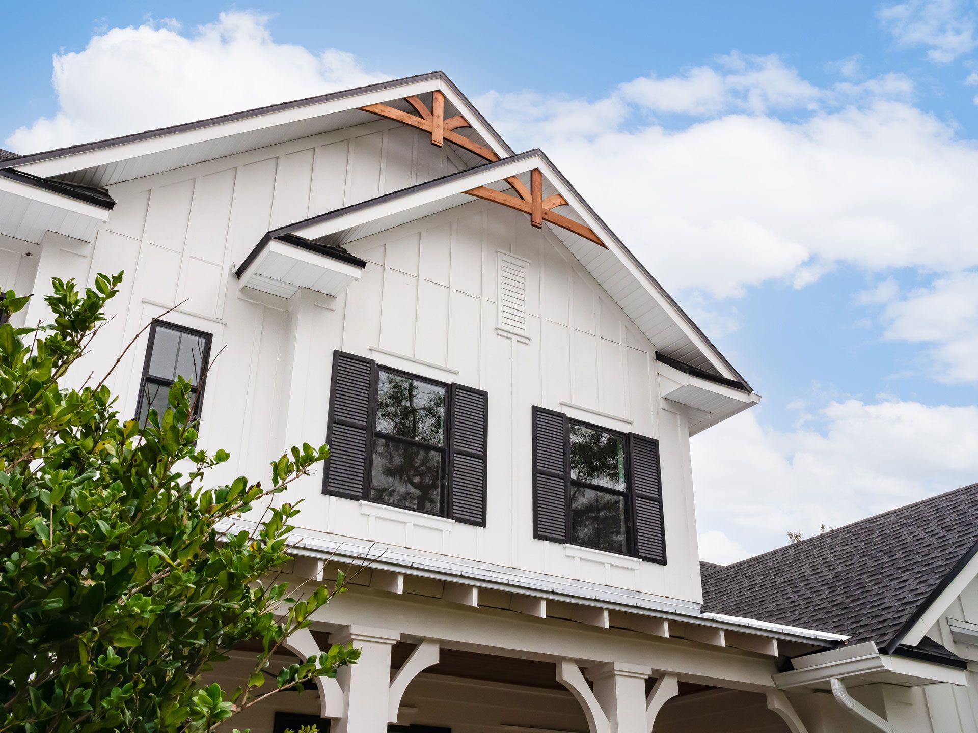 White house with black shutters, dark roof, and wooden accents against a blue sky.