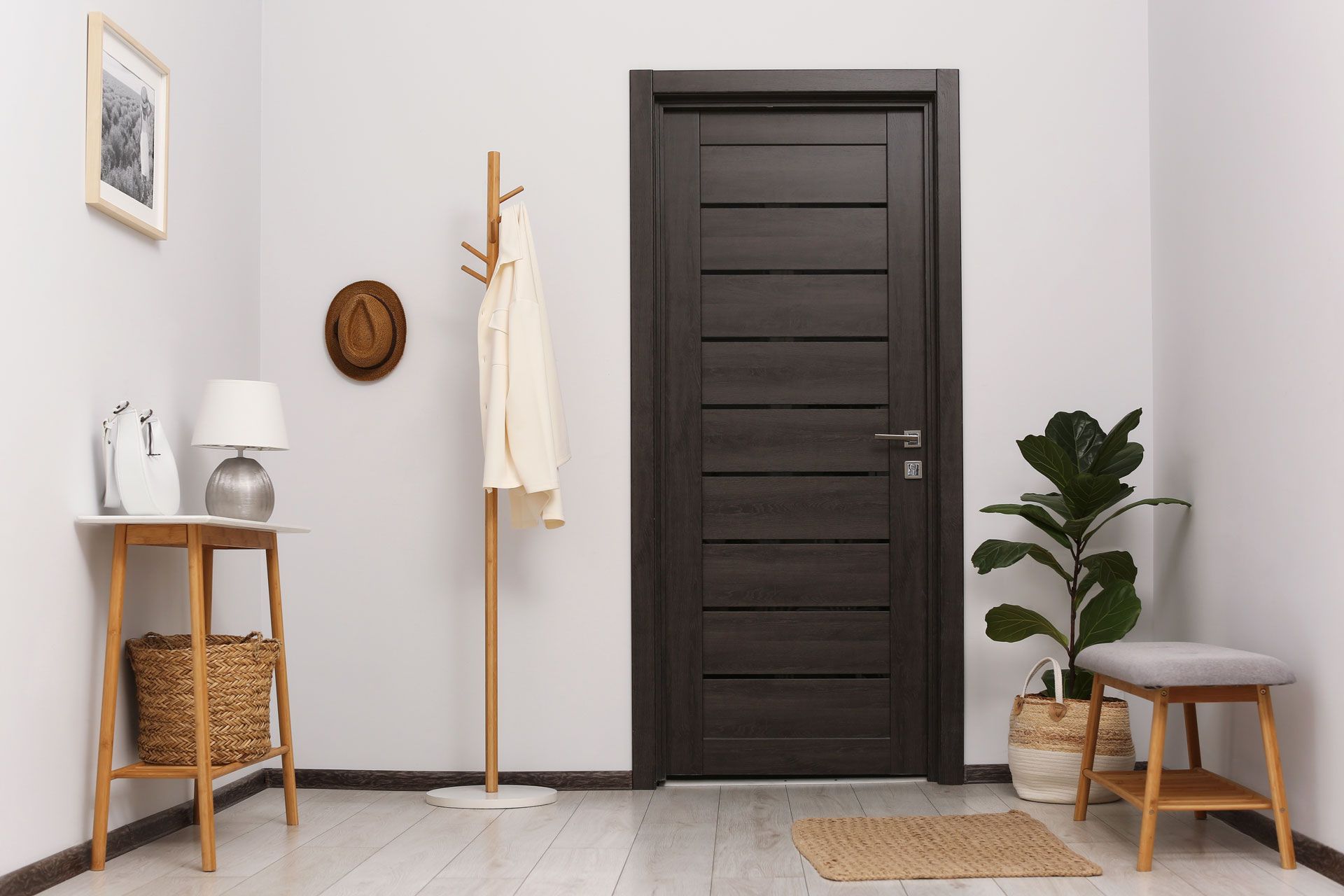 Hallway with dark brown door, coat rack, table, bench, and potted plant. White walls, wooden floor.