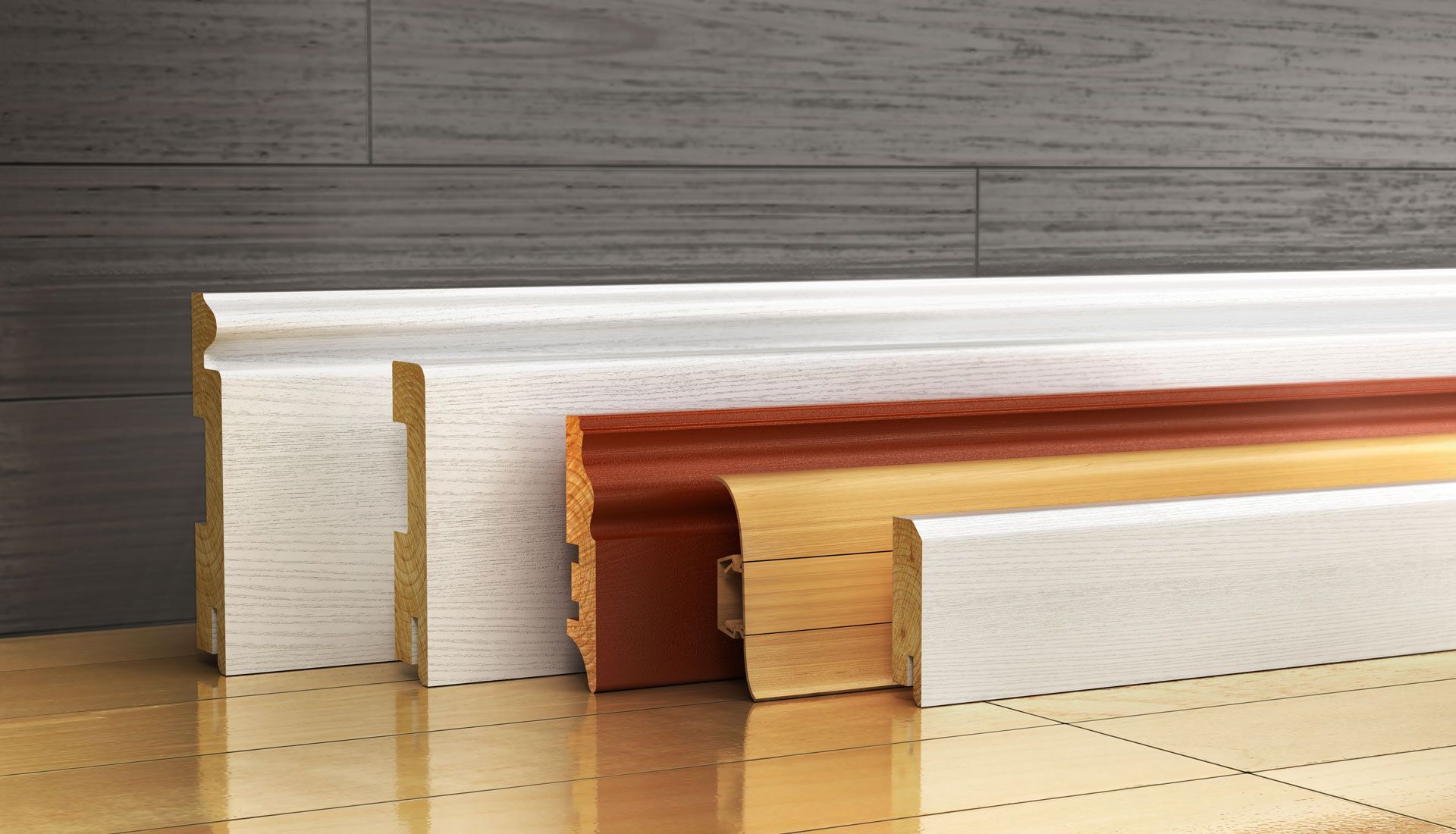 Baseboards, wooden molding samples in white, brown, and natural finishes, resting against wood flooring and wall.
