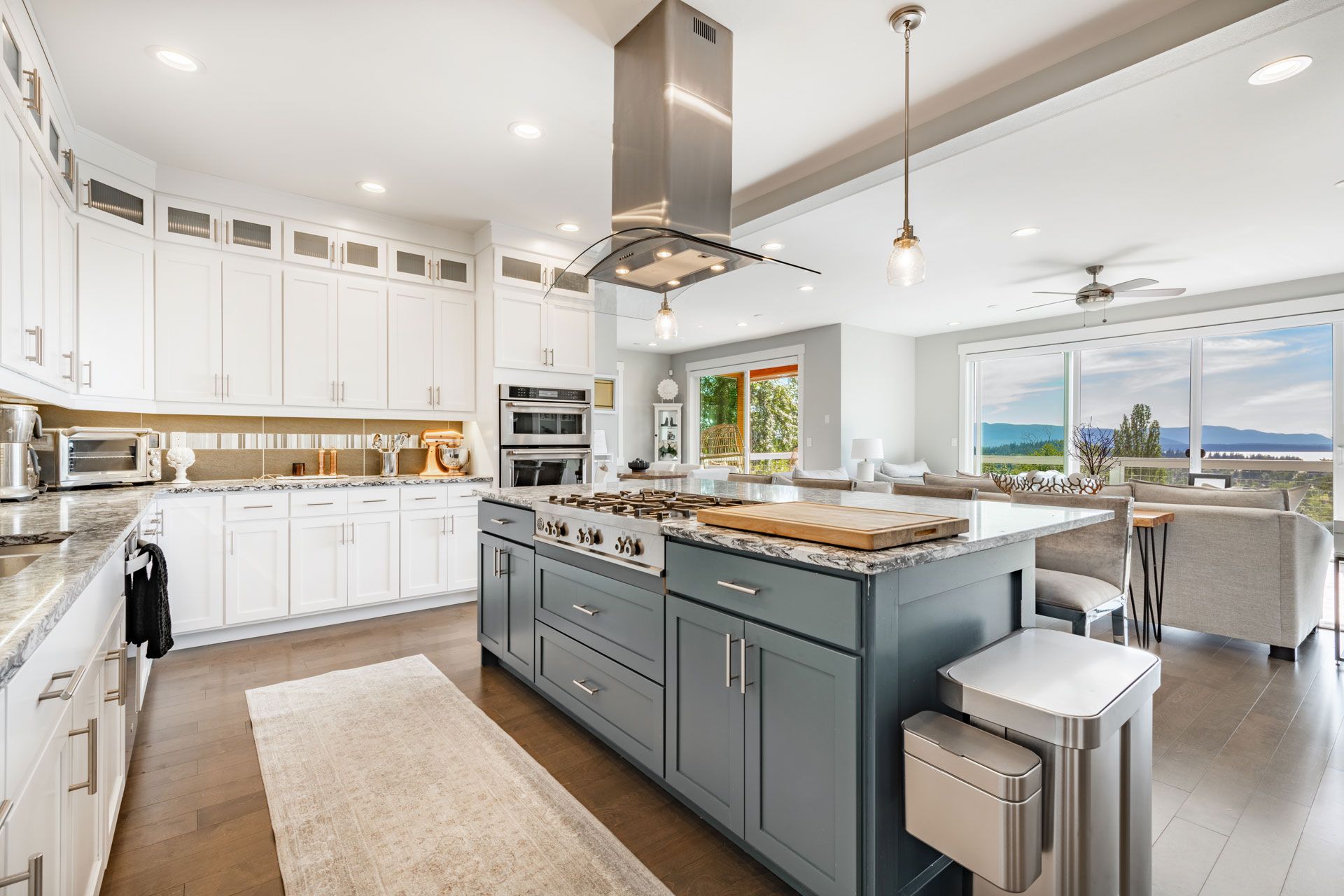 Spacious kitchen with blue island, stainless steel appliances, white cabinets, and living area with window.