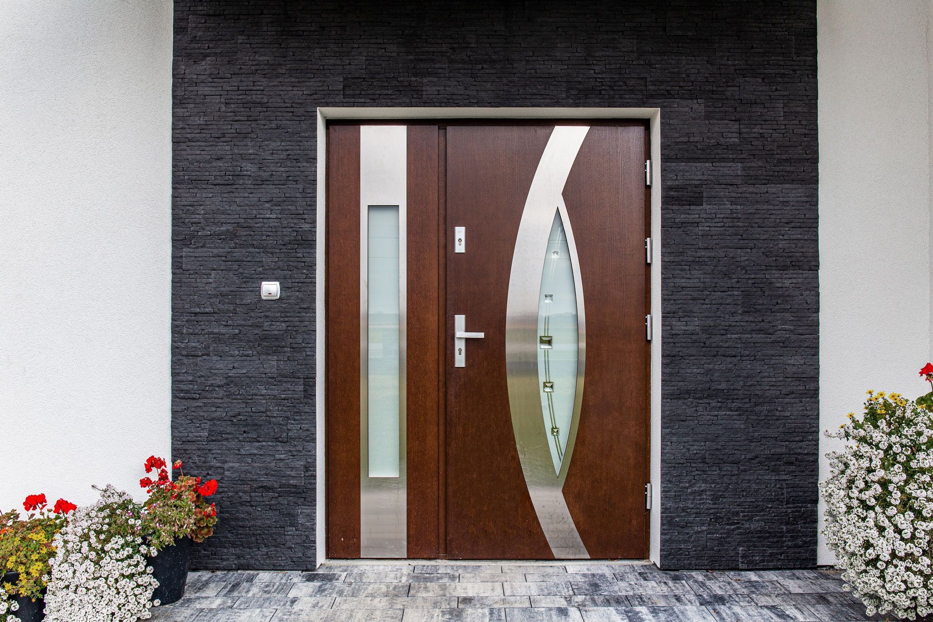Brown double door with glass panels and silver accents, set in a black stone wall.
