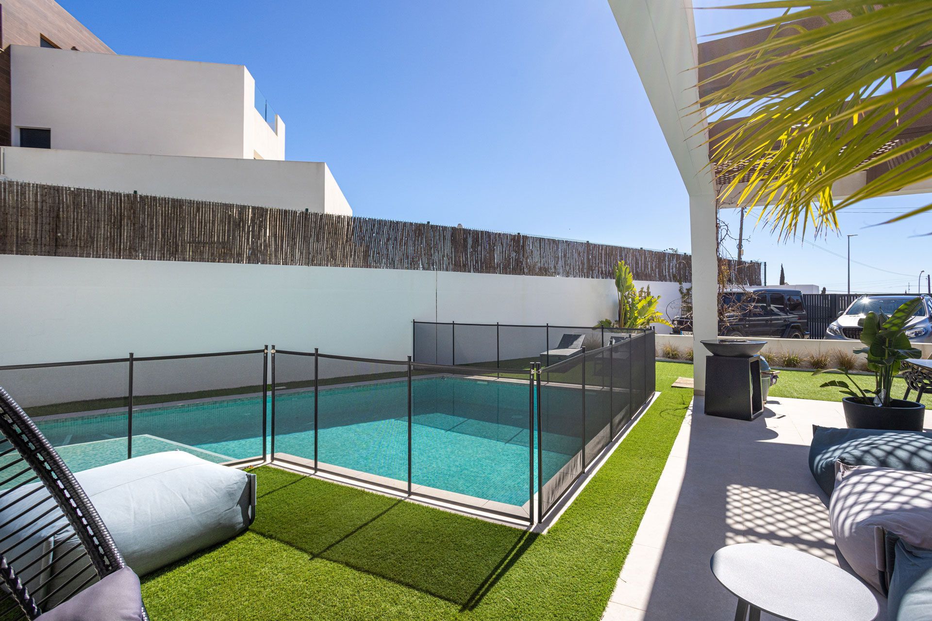 Pool area with pool, black safety fence, and patio furniture.