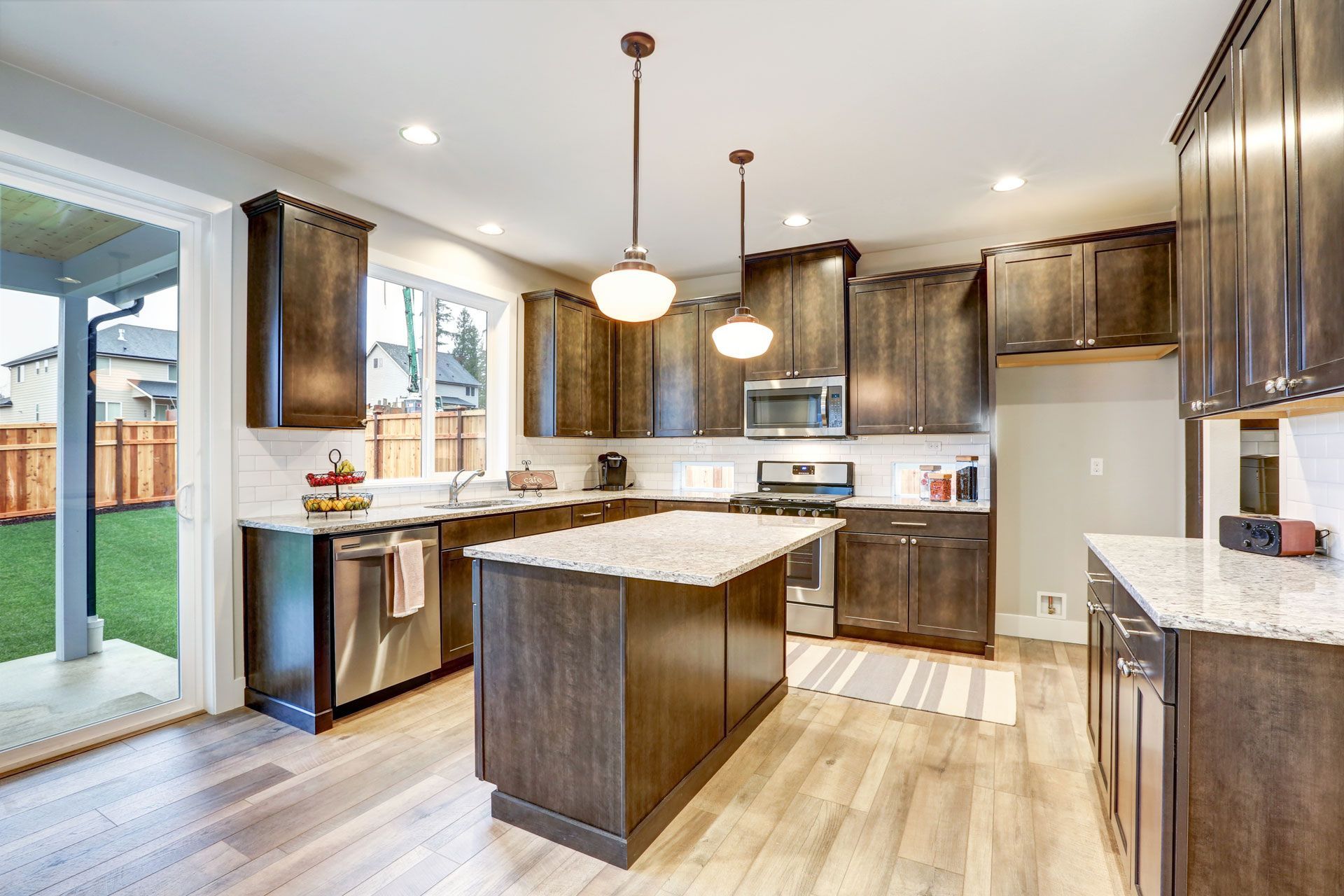 Kitchen with brown cabinets, island, and stainless steel appliances. Sliding glass door leads to backyard.