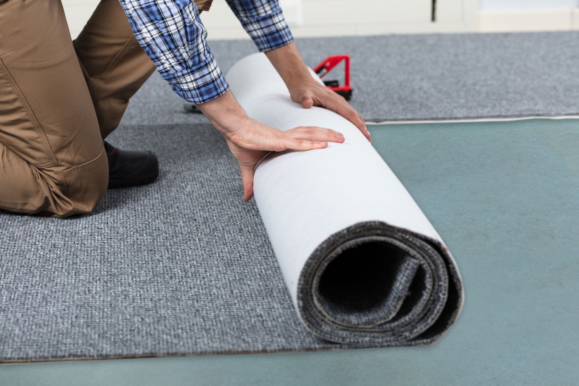 Person unrolling gray carpet onto floor, showing the white backing.