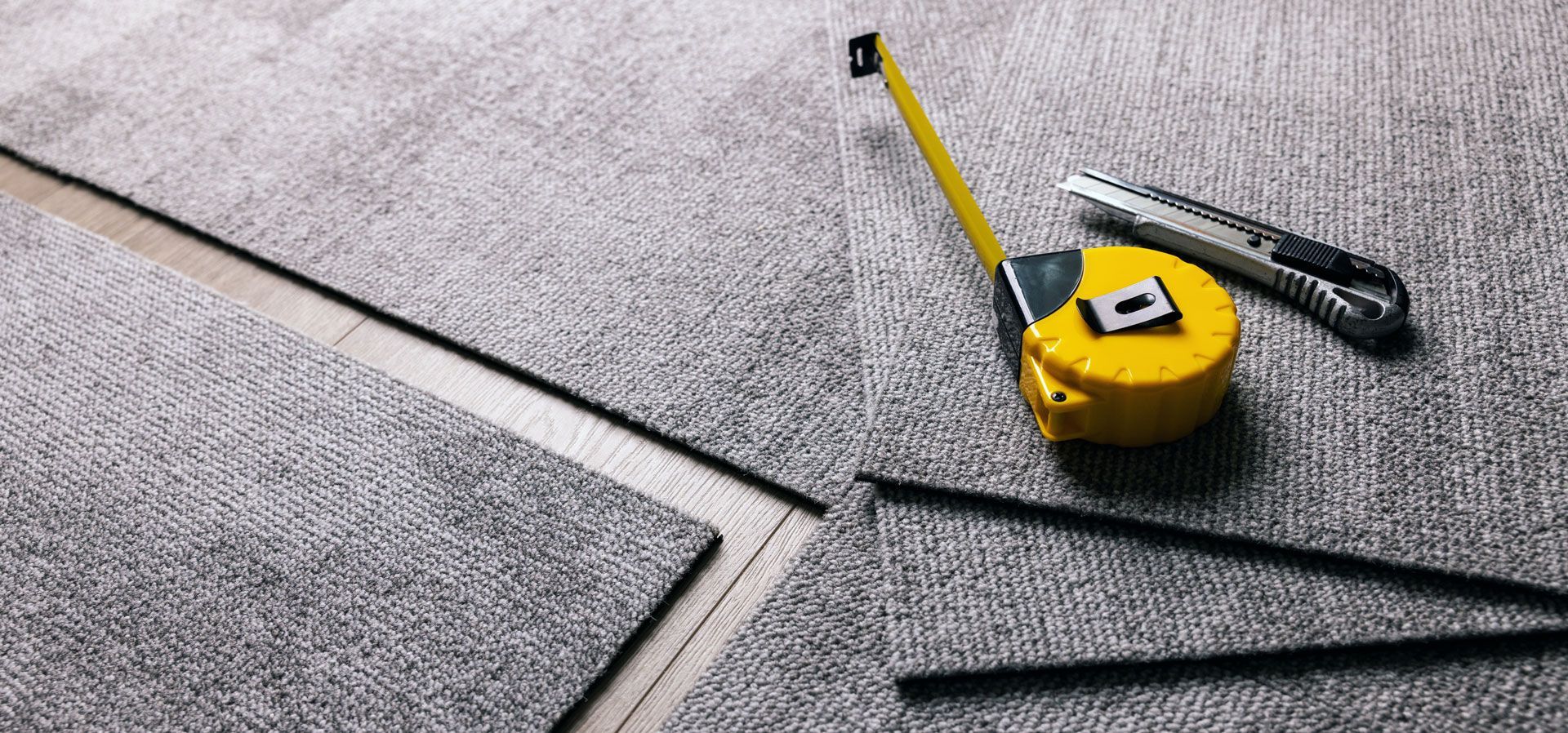 Tools for cutting carpet: tape measure, utility knife, and carpet tiles.