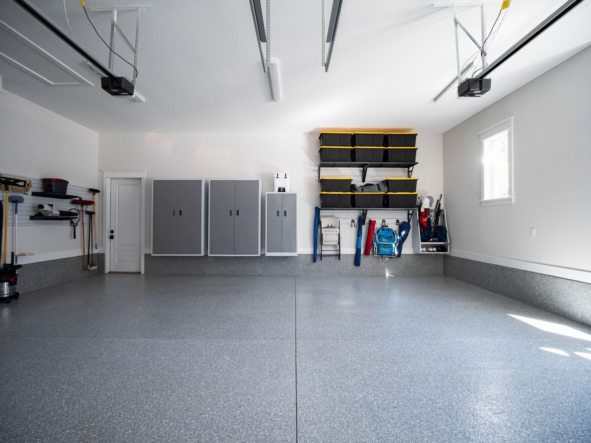 Clean, organized garage with epoxy floor, cabinets, storage bins, and tools.