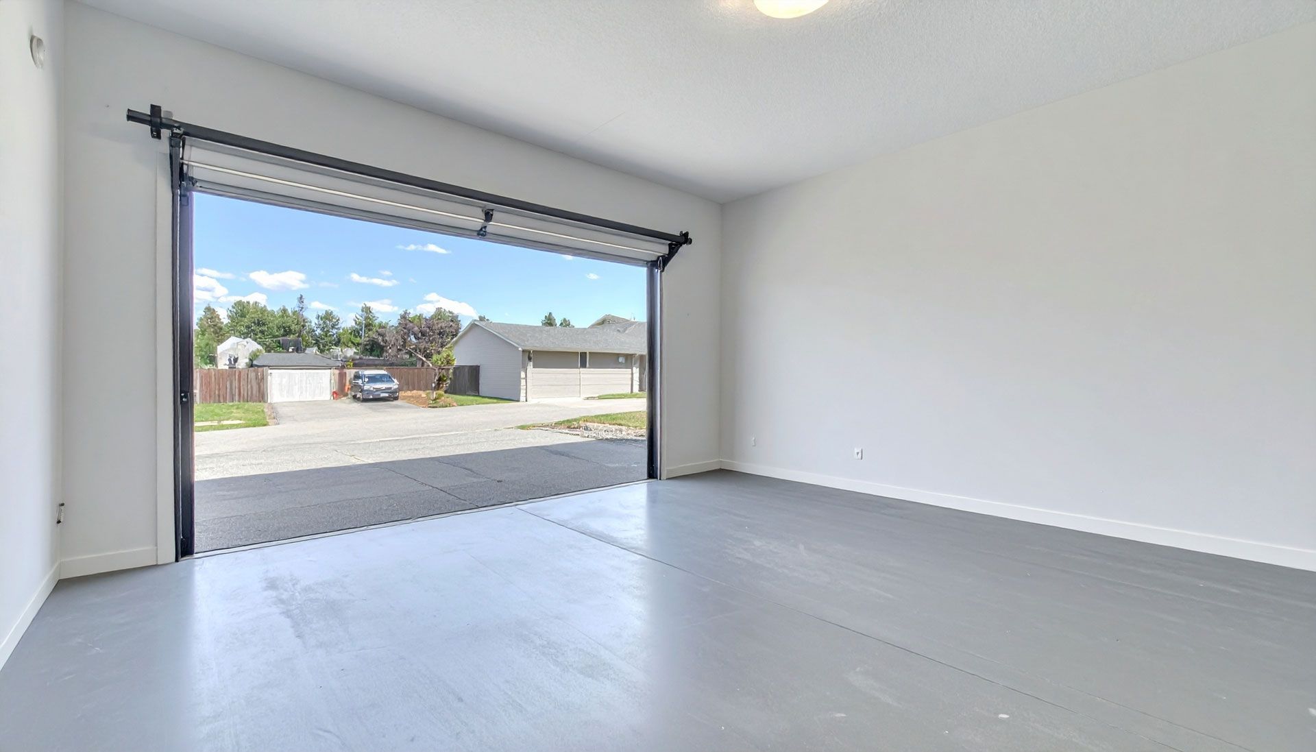 Empty gray garage with open door looking out to a street and homes.