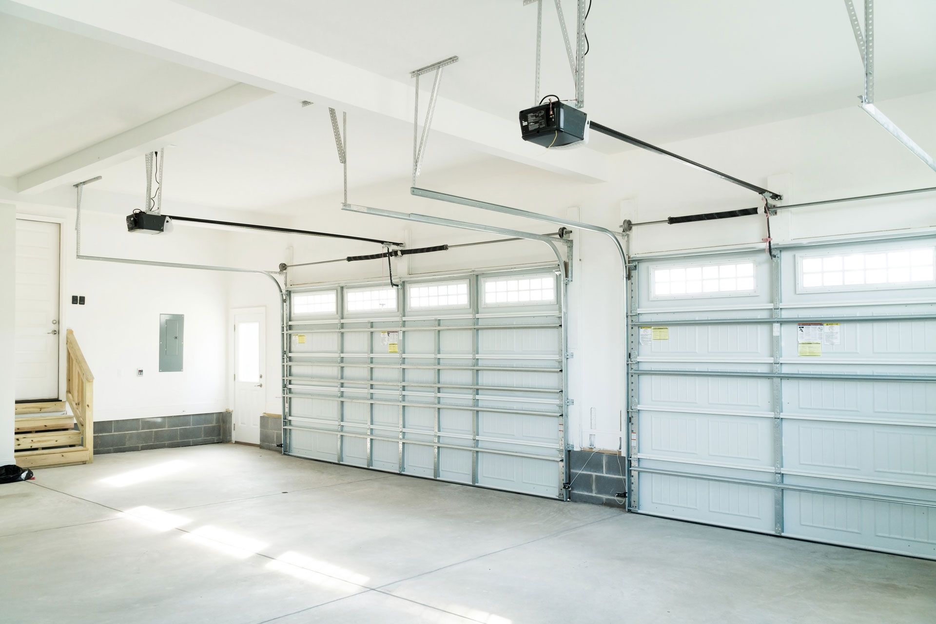 Empty, white-walled garage with two overhead garage doors, each with a windowed top section and metal framework.