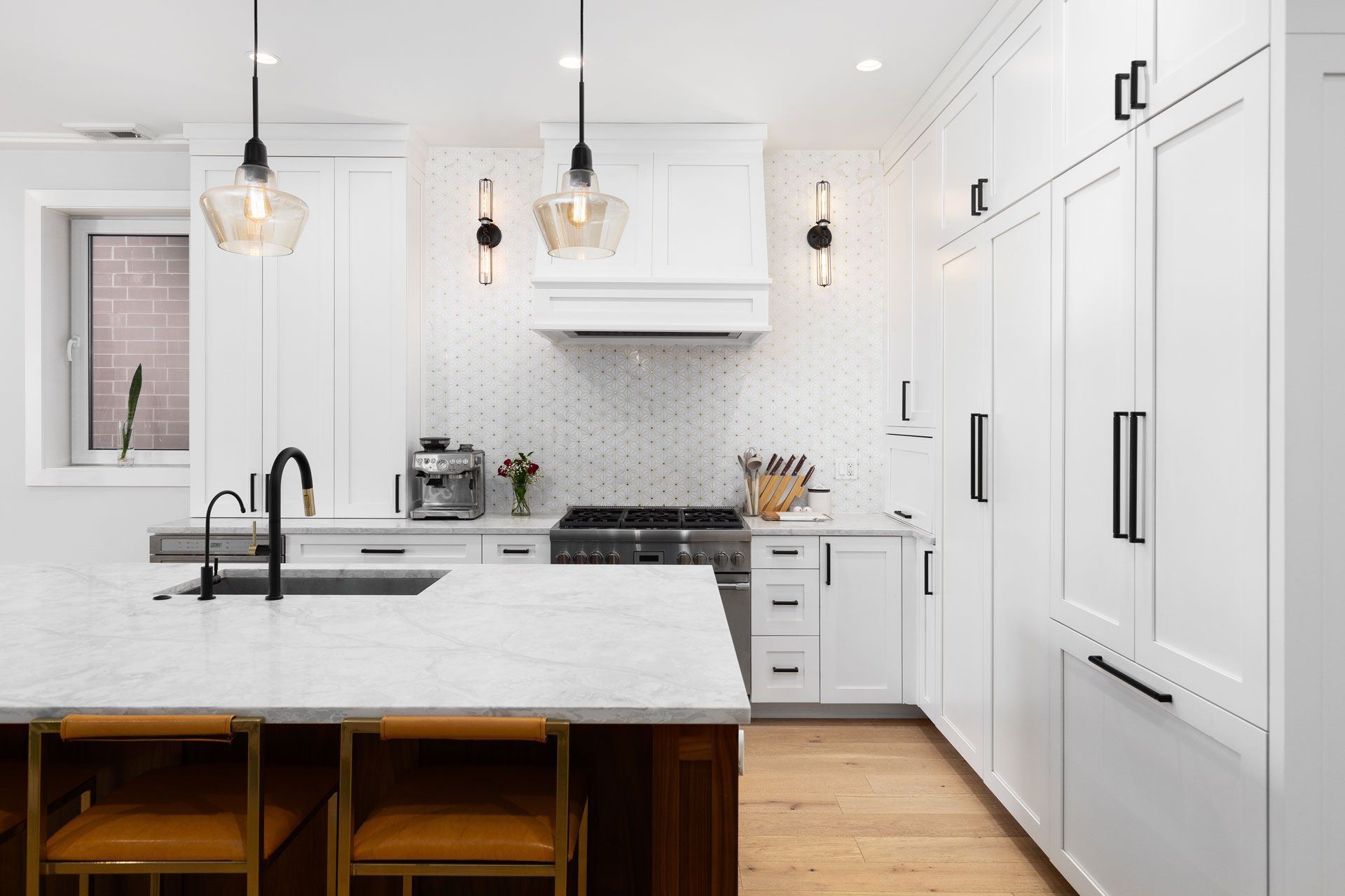 Modern white kitchen with island, marble countertops, pendant lights, and stainless steel appliances.