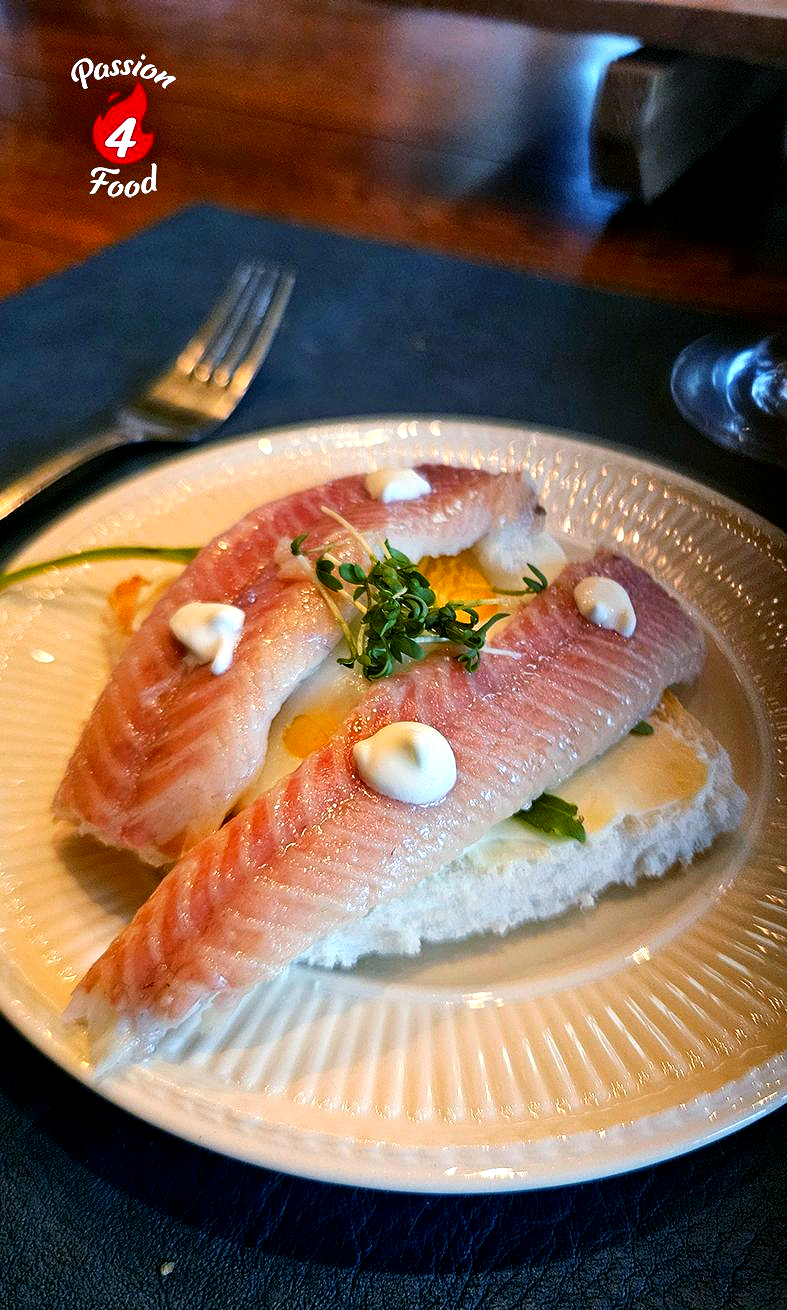 Twee filets van witte vis geserveerd op brood met een klodder witte room en verse kruiden op een wit bord.