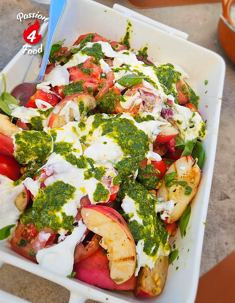 Een schaal met een kleurrijke salade met tomaten, komkommer, perziken, kruiden en een dressing.