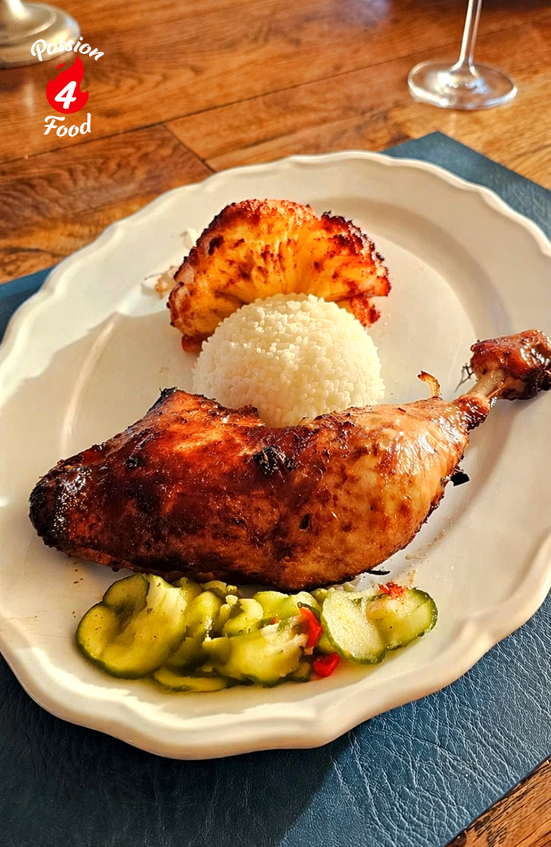 Een bord met gegrilde kip, rijst en plakjes komkommer op een eettafel.