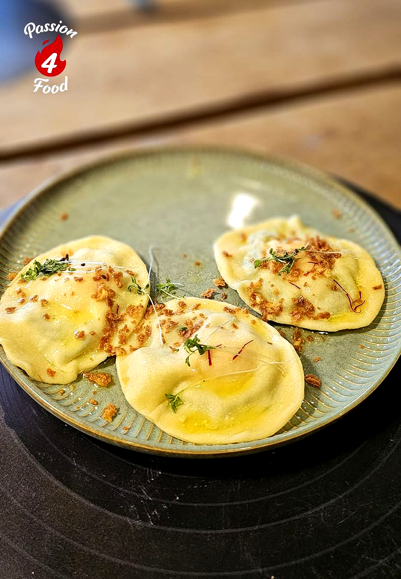 Een bord met vier met kruiden gevulde ravioli op een groen bord op een houten tafel.