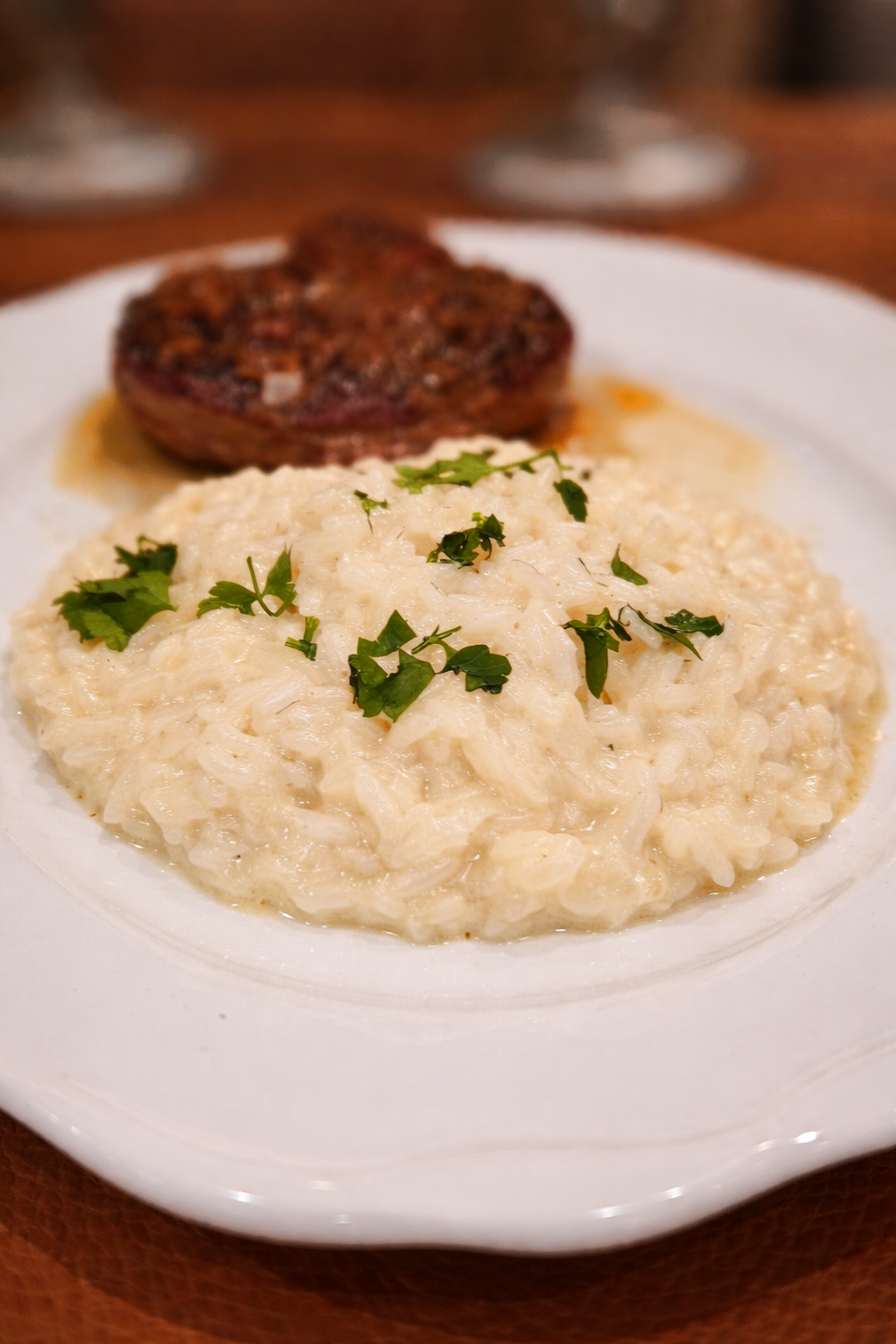 Risoto al burro e pamigianp reggiano op wit bord met kalfsschenkel en een beetje jus.