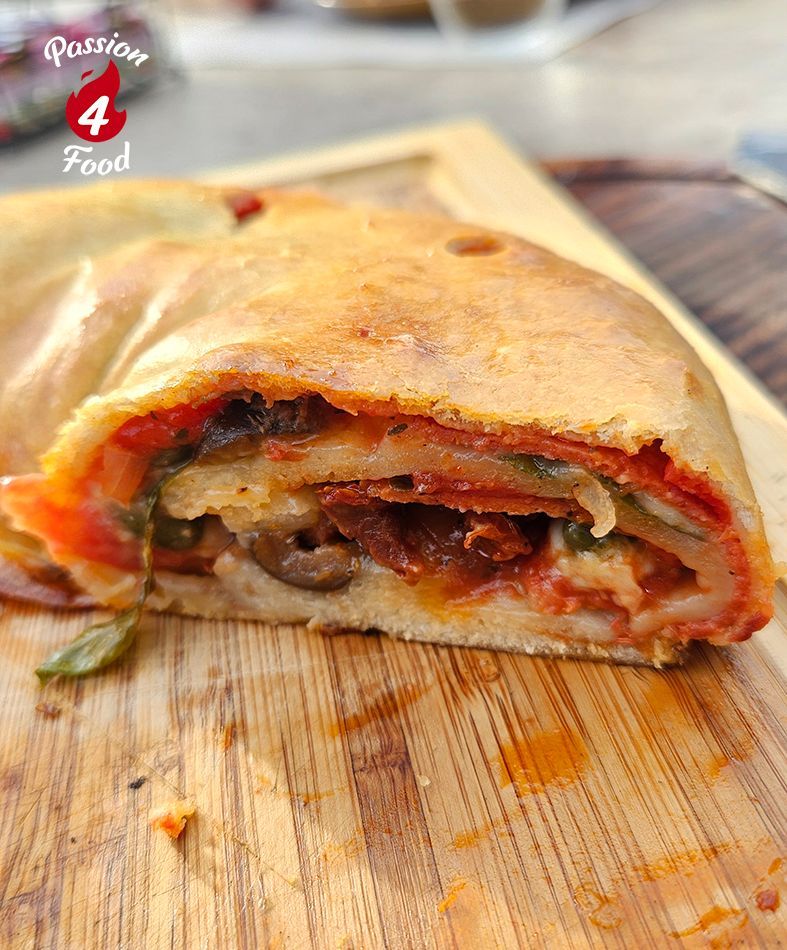 Close-up van een doorgesneden, gevulde pizzarol met gesmolten kaas op een houten plank.
