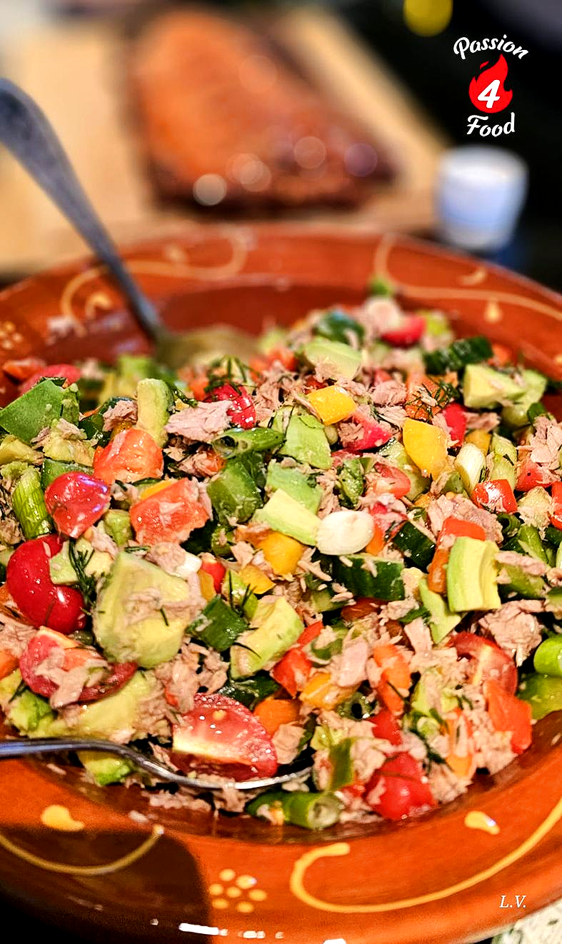 Een kom met grove tonijnsalade, avocado, tomatenblokjes en paprika in een rustieke, oranje kom met patroon.