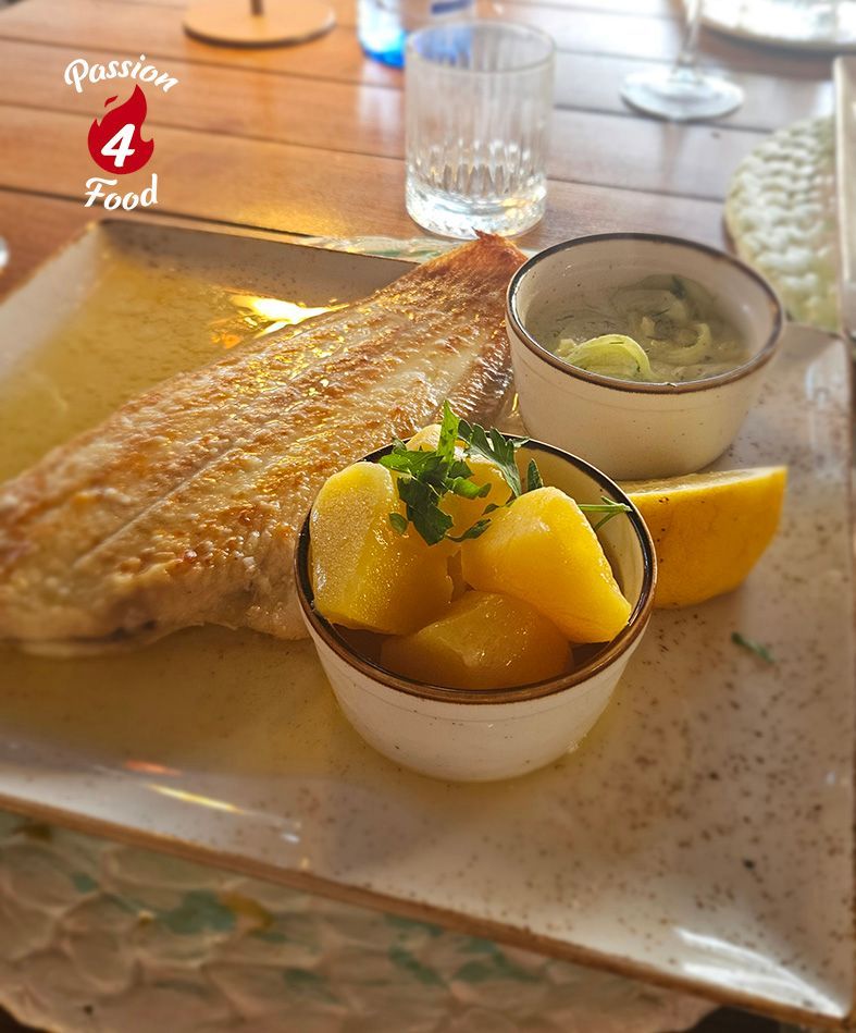 Grilled fish with parsley patotoes and cumcumber on a white plate at a restaurant table