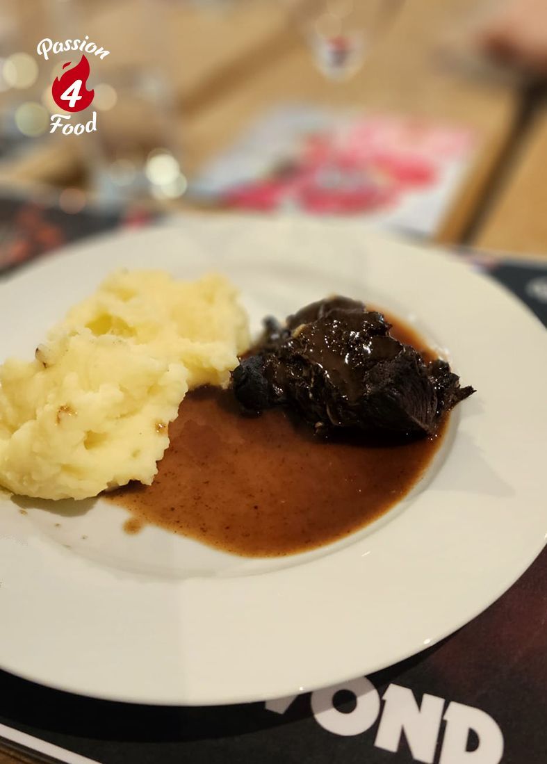 Gestoofde runderwang in rode wijn met truffelaardappelpuree op wit bord.