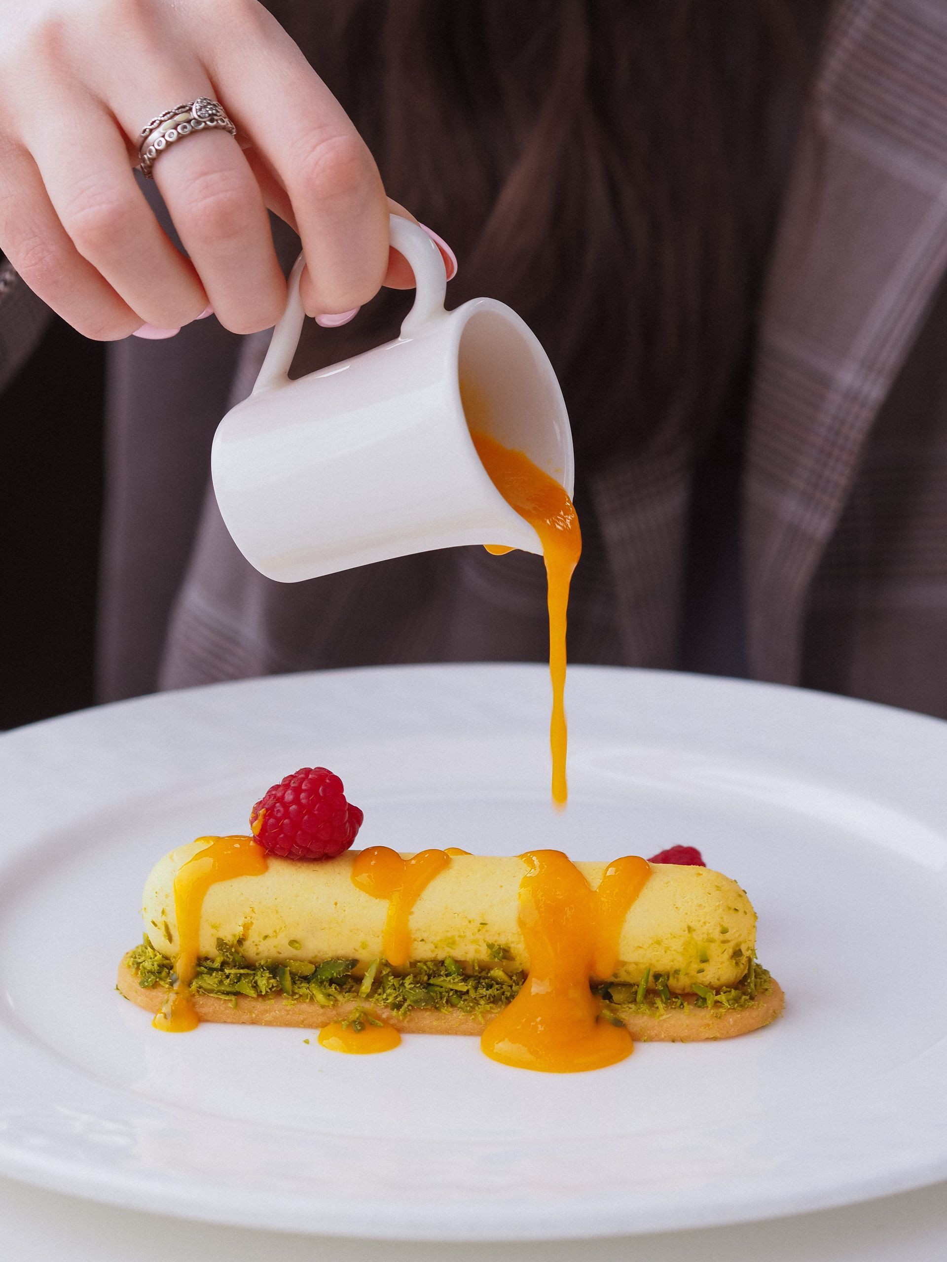 Met de hand mangosaus over een op een bord geserveerd dessert gegoten, gegarneerd met  frambozen