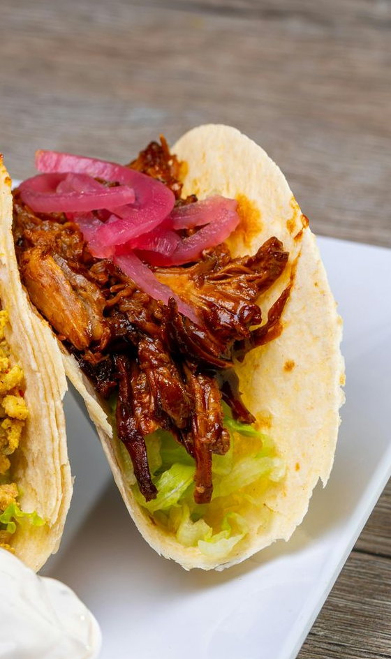 Taco met pulled pork, ingelegde rode uien en groene salsa op een wit bord.