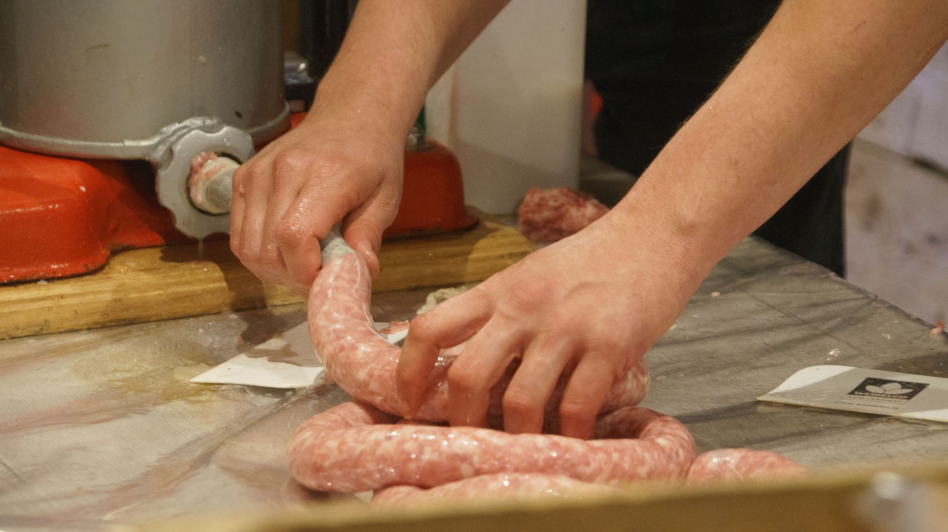 Hands twisting raw sausage on a kitchen counter near a meat grinder.