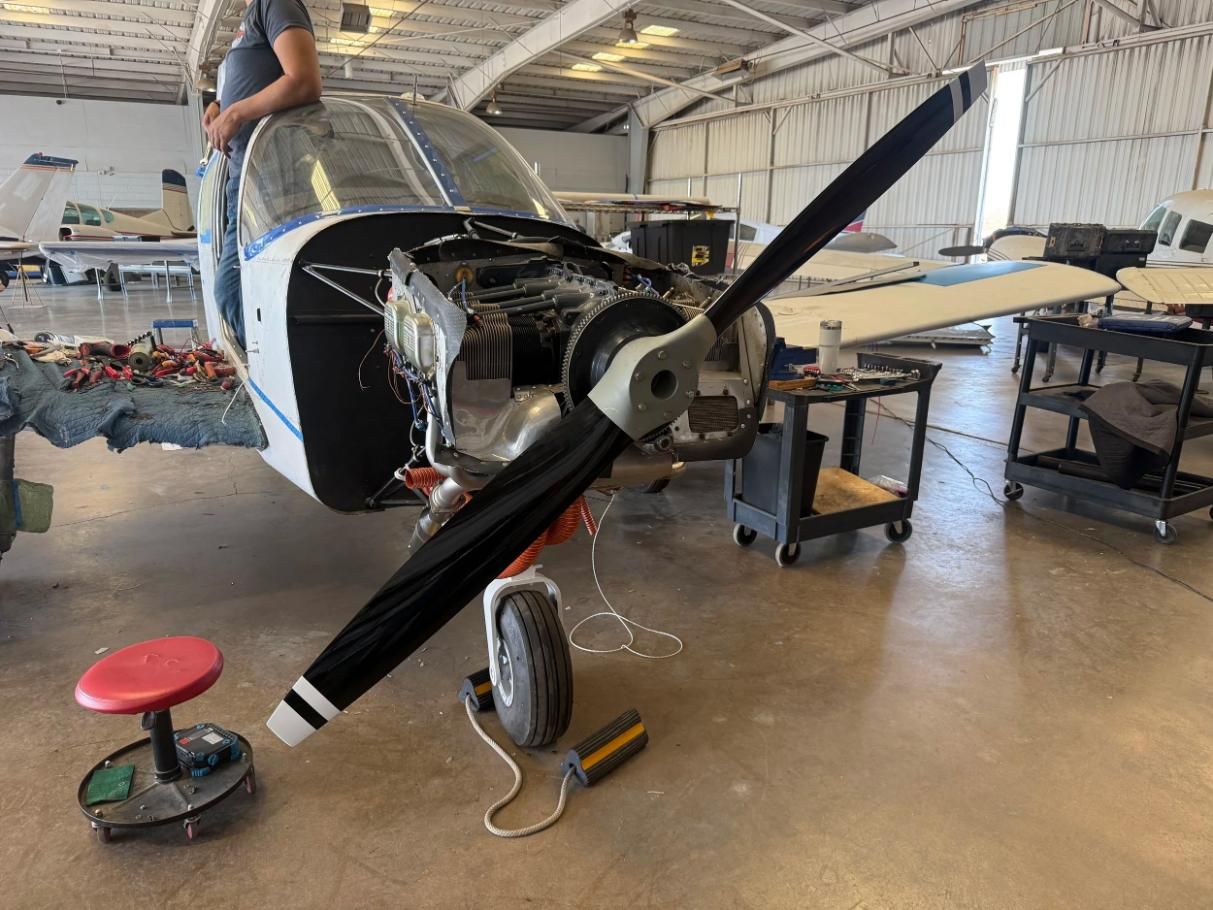 Small aircraft in workshop with exposed nose and propeller, tools and equipment nearby