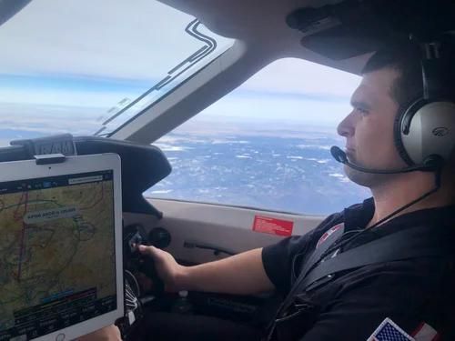 Pilot in cockpit wearing headset, flying over snowy landscape with navigation display visible.