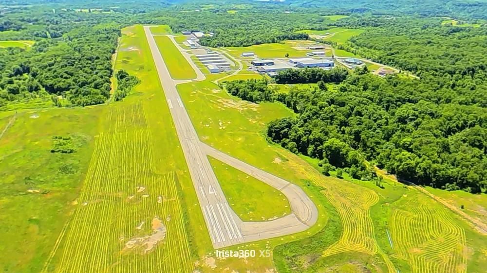 Aerial view of a small airport runway surrounded by green fields and dense forest.